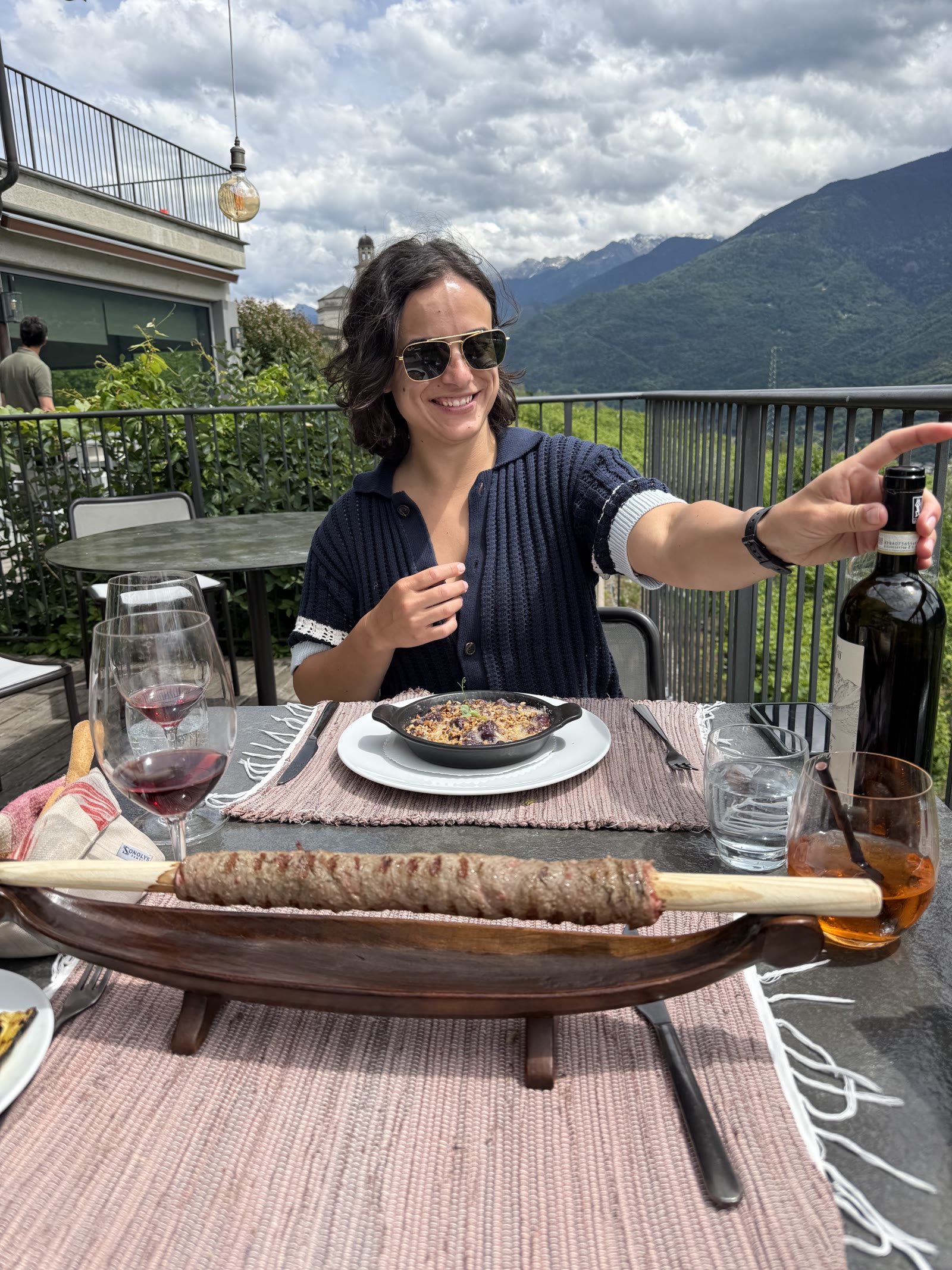 Sarah Mifsud sharing wine at a table in the mountains